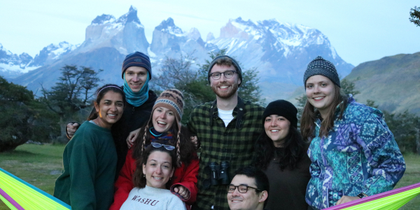 students cluster in and around a hammock in front of a mountain range